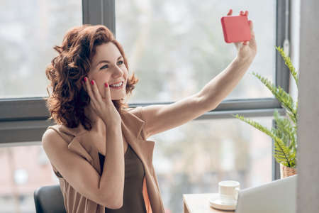 Young woman sitting near the window and making selfie