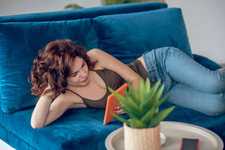 Woman laying on a sofa with a tablet in hands