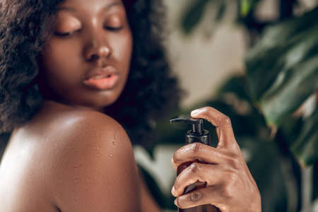 Naked dark-skinned young woman applying body lotion on her bodyの写真素材