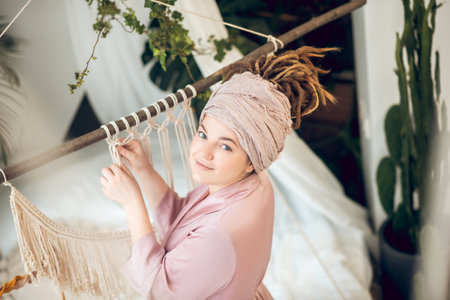 Young woman in a headwear weaving macrame and looking positiveの写真素材