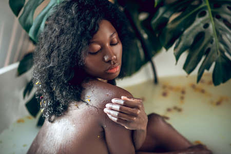 Dark-skinned beautiful naked woman enjoying a bath and looking relaxed