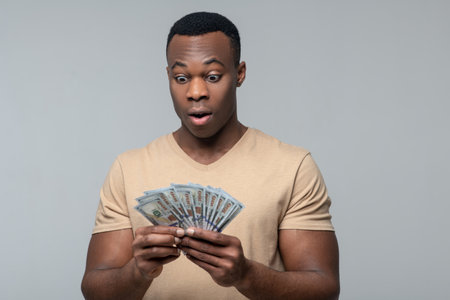 Surprised dark skinned man looking at banknotes