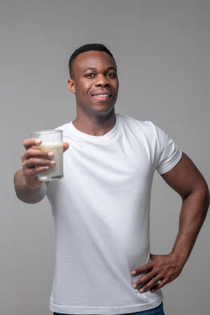 Cheerful man holding out glass of milk forwardの写真素材