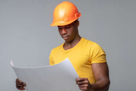Serious man in helmet considering blueprint drawing