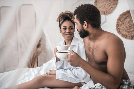 Woman and man with coffee sitting on bedの写真素材