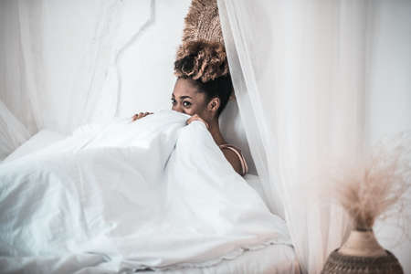 African american woman under white blanket in bedの写真素材