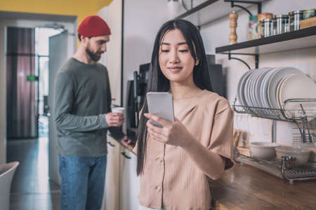 Cute asian girl having coffee with colleagues and textingの写真素材