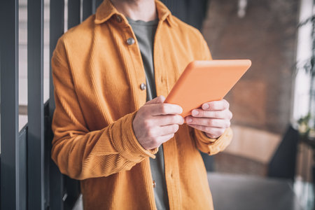 A man in an orange jacket with a tablet in handsの写真素材