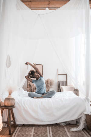 Woman sitting on bed bends to sideの写真素材