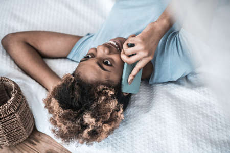 Smiling woman talking on smartphone lying on bed