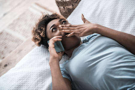 Surprised woman with smartphone covering mouth with handの写真素材