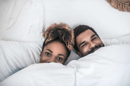Smiling man and woman lying under blanketの写真素材