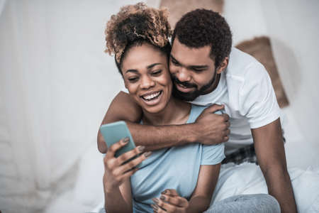 Man hugging woman sitting with smartphone