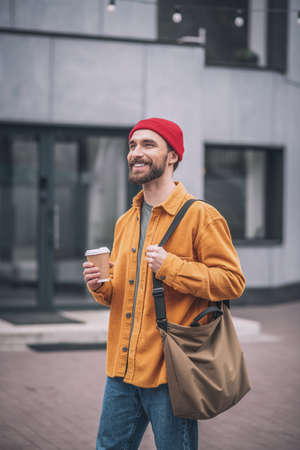 Man in a red hat and orange jacket with a coffee cup in handsの写真素材