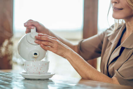 A pretty woman pouring tea from the tea pot to the cupの写真素材