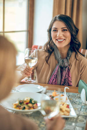 Smiling young woman holding a glass of wine and toasting with friendsの写真素材