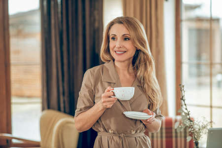 Long-haired elegant woman having tea and looking contented