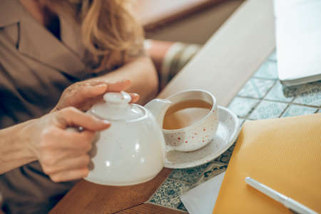 Woman pouring tea to the cup from a white tea potの写真素材