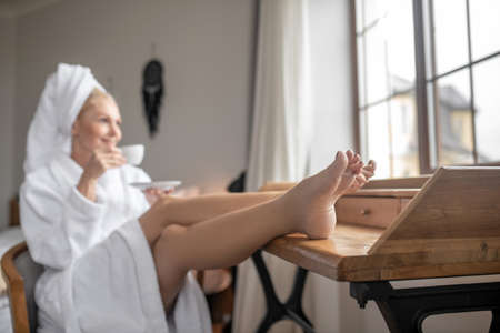 Beautiful woman in a white robe having coffee after the bathの写真素材