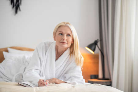 A cute woman lying on the bed and making notesの写真素材