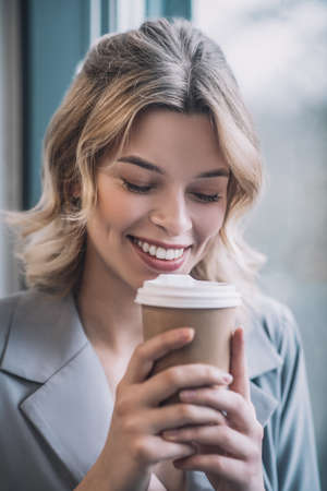 Smiling woman with drooping eyelids bringing coffee to faceの写真素材