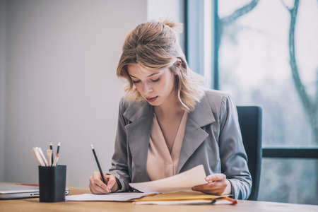 Focused woman taking notes on documents in officeの写真素材