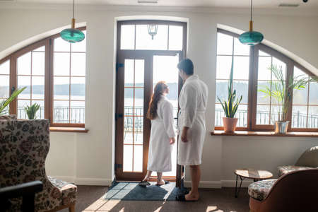 A couple in white bathrobes standing near the window and looking romanticの写真素材