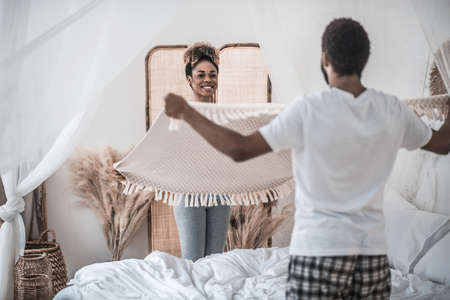 Darkskinned woman and man standing with blanket near bed
