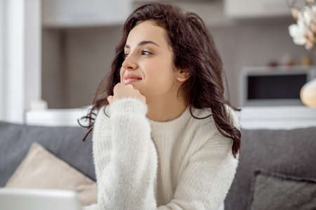 Young woman sitting on the sofa with a laptop and looking relaxed