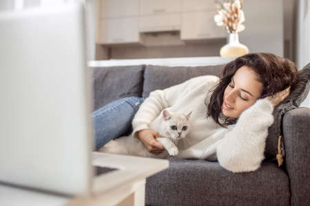 Young woman laying on the sofa with her cat and looking relaxedの写真素材