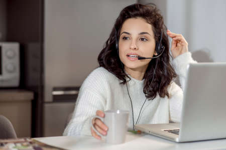 A woman in earphones sitting at the laptop while working from home