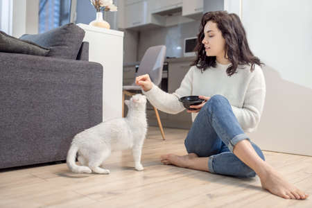 Dark-haired lovely woman feeding her white cat
