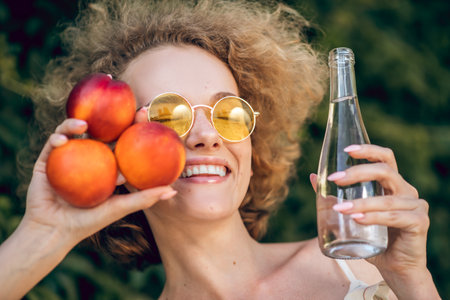 Curly-gaired young woman with nectarines looking happyの写真素材