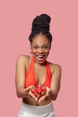 Mulatta in orange top holding strawberries in her handsの写真素材