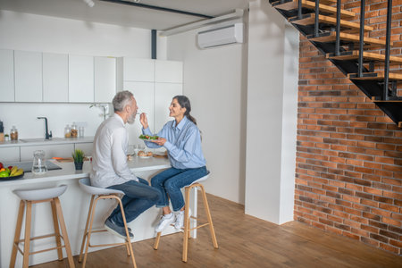 Dark-haired young woman feeding her husband and smilingの写真素材