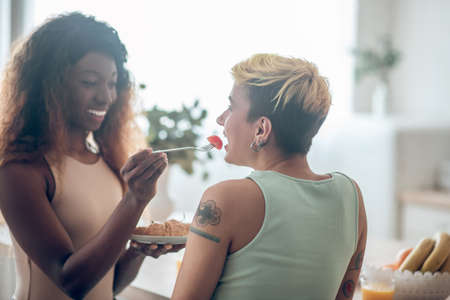 Dark-skinned woman feeding caucasian girlfriend with tomatoの写真素材