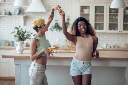 Caucasian woman holding hand of dark-skinned dancing girlfriendの写真素材