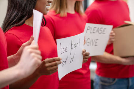 Hands of volunteers holding posters calling for participation in charityの写真素材
