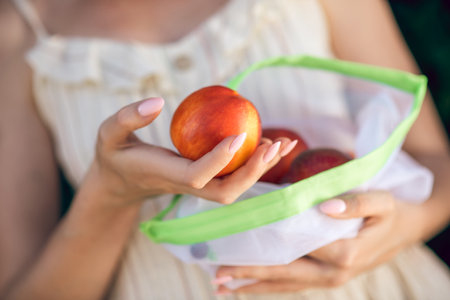 A picture of a woman in a light dress with a nectarine in her handの写真素材