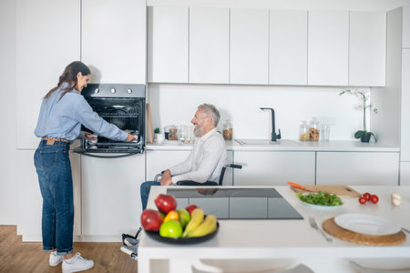 Gray-haired handicapped man and his young wife in the kitchen getting the breakfast readyの写真素材