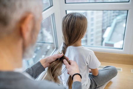 A gray-haired dad doing hair to his daughterの写真素材