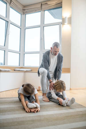 Father training his kids at home making them stretch correctlyの写真素材