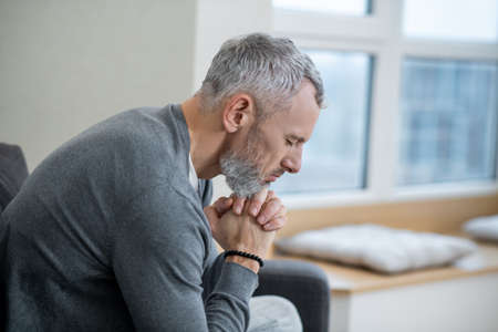 A gray-haired man sitting with eyes closed and saying the payers