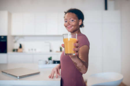 A dark-skinned woman holding a glass of orange juice