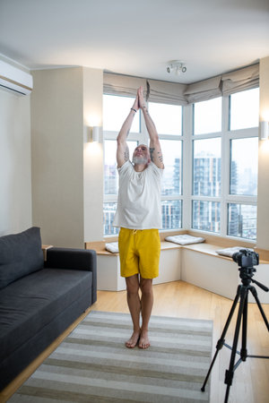 A mature man in white tshirt doing yoga tutorial onlineの写真素材