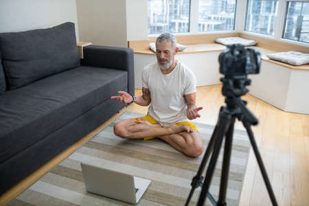 A mature man in white tshirt doing yoga tutorial online