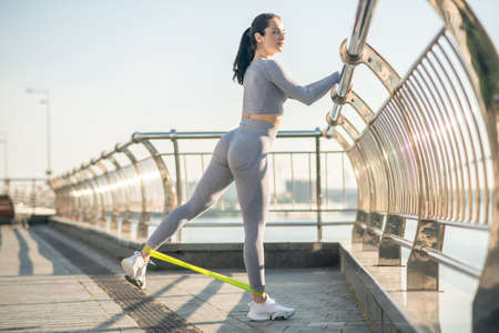 Female sportsperson in grey sportswear exercising with a resistance band