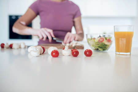 A dark-skinned woman cooking in the kitchen and cutting vegetablesの写真素材