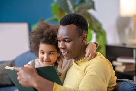 Daughter hugging by neck dad reading book