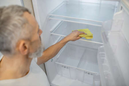 A gray-haired man cleaning the fridge in the kitchenの写真素材
